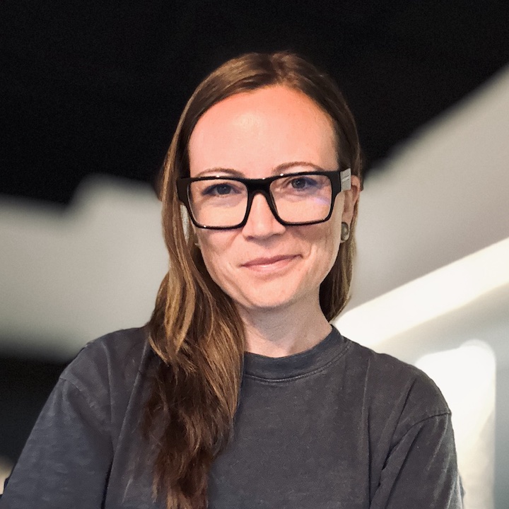 Lindsay Moore, smiling, in black-framed glasses and a charcoal shirt.